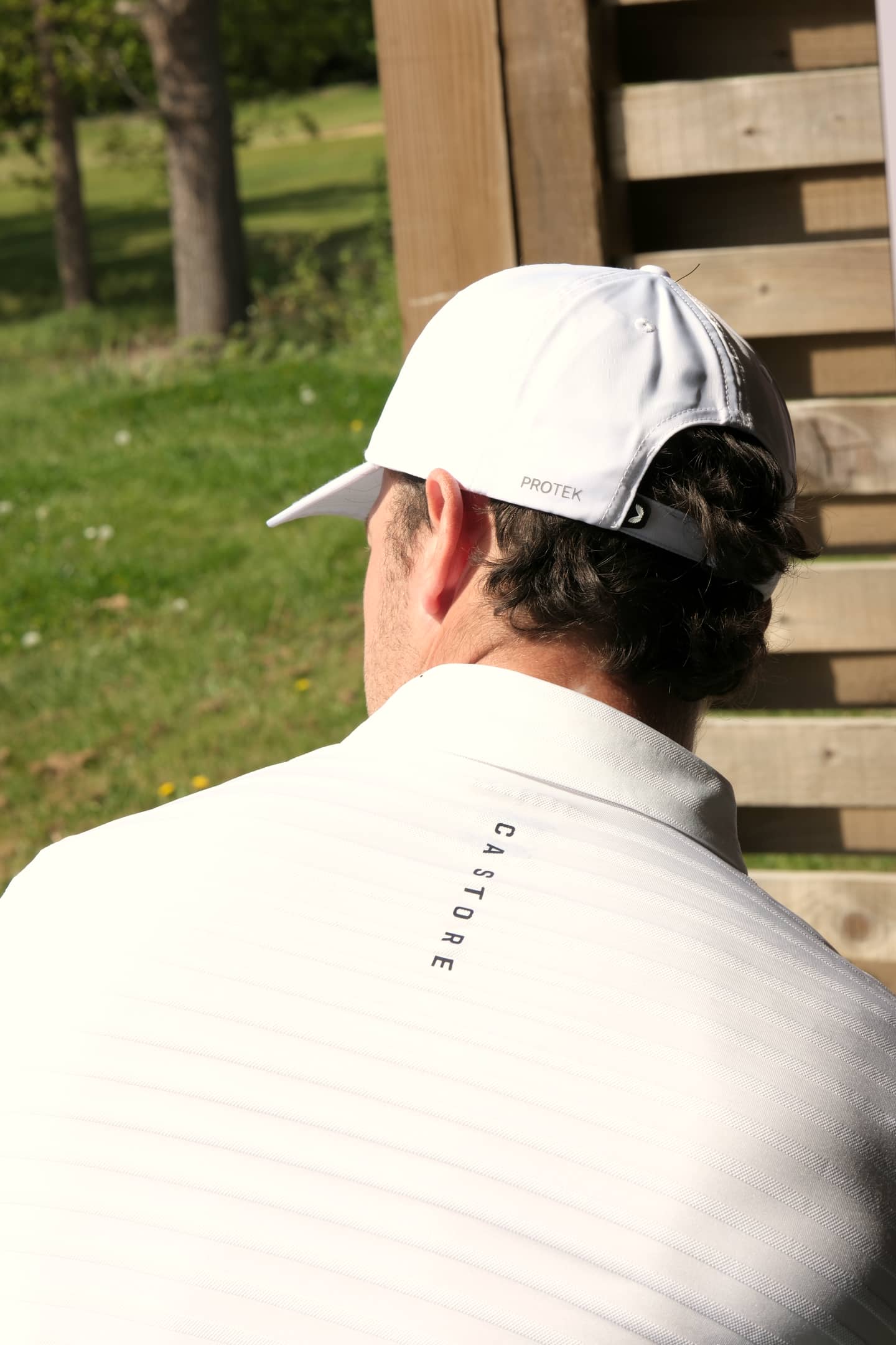 Huw Williams from behind in the coaching bay, cap and Castore shirt, course beyond