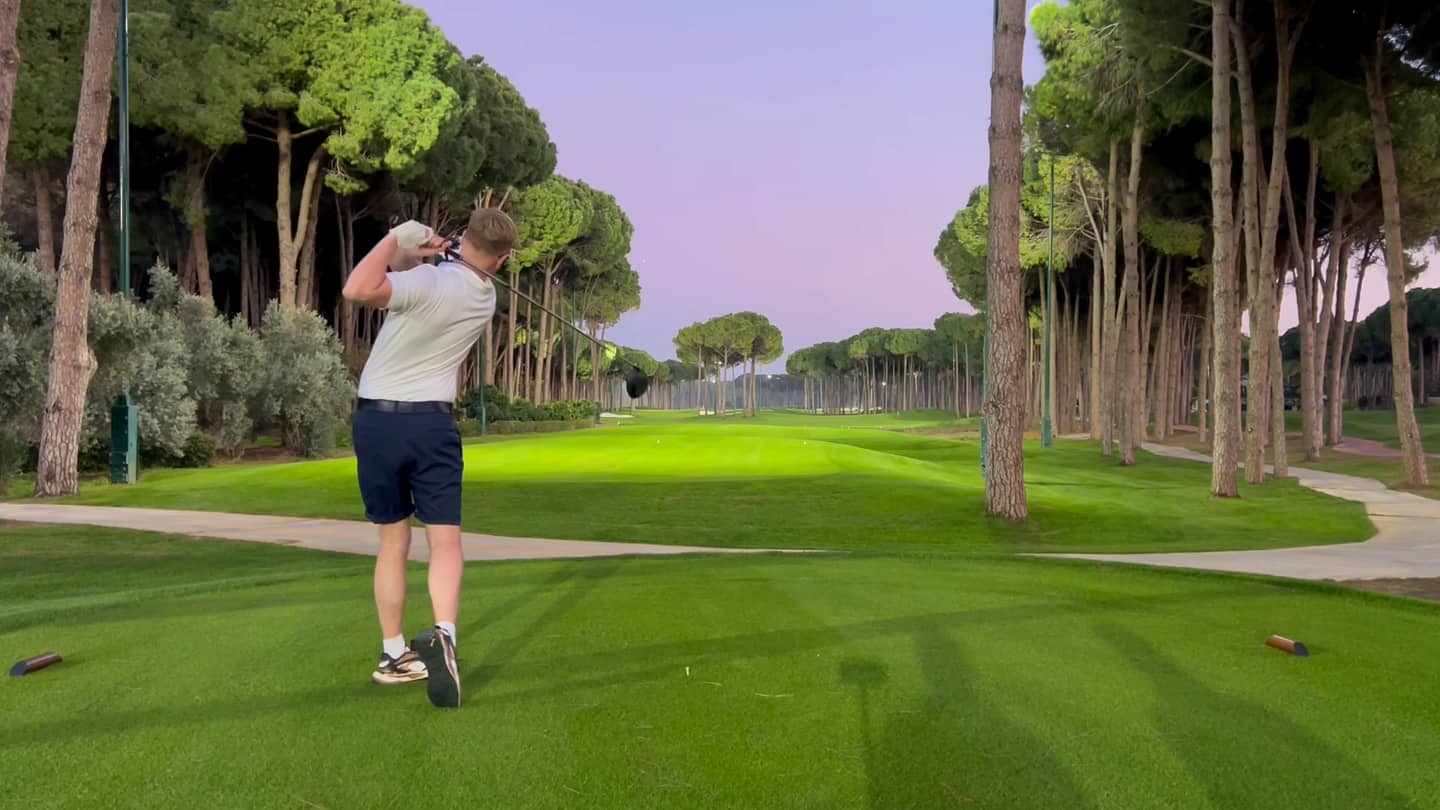 A floodlit pine-lined course at dusk, Huw Williams holding his finish