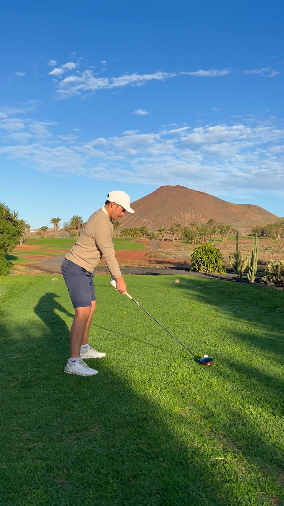 Huw Williams at address with a driver at golden hour on a resort course, a volcanic hill behind